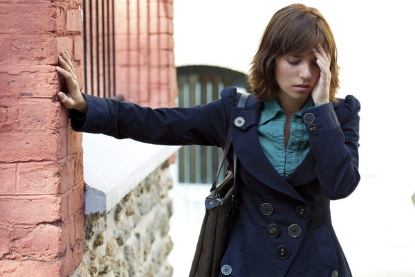 A woman experiencing dizziness outside leaning on a wall